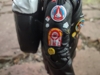 A close up shot of Ace's right arm, showing off the various 'pins' and 'patches' on that part of her jacket. Details that are identifiable are a white smiley face, a yellow smiley face, and what looks to be a NASA mission patch