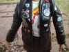 A close up shot of Ace's torso, showing off the various 'pins' and 'patches' on that part of her jacket. Details that are identifiable are an American flag, a patch that reads 'Ace Roofing Go Lee', what appears to be a 'pin' of half a British flag, and a Blue Peter badge