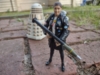 A photograph of Ace wielding her rocket launcher accessory with the Dalek in the background, patrolling