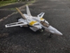 A KO of the Takatoku 1/55 scale VF-1S in fighter mode. It is a white fighter jet with yellow detailing on the fuselage and vertical stablizers and a lback stripe going down the wings, with the letters GS-11 on the stripe of one wing and an emblem on the stripe of the opposite wing - said emblem is an upside down exagon with a three pointed star inside of it with an upside down triangle in the center