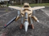 The VF-1A in gerwalk mode - effectively a midway transformed mode where the legs and arms are deployed but the rest of the jet remains untransformed. The gun pod (the standard firearm for gerwalk and battroid mode) is being wielded.