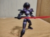 A model kit action figure of an Acerby (Type E) - a female robot. She is colored black, purple, and violet and has a red transparent visor over her face. She has shoulder pads on and is wielding a sword with a transparent red blade in one hand and a shorter dagger with a transparent purple blade (that you can't see thanks to the angle but trust me - it's there) in other hand and is standing in a wide stance-