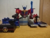 AOTP Star Convoy in base mode, in the official configuration (per the instructions). His upper body is pretty much fully in robot mode, albeit with the head facing down, he is wielding his gun in one hand and sword in the other hand, Hot Rod is manning a turret on a platform to his left (the viewer's right) and the Micro Trailer in battle platform mode is placed in front of the right section (viewer's left)