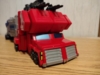 Age of the Primes Star Convoy in truck mode, a red futuristic truck hauling a grey trailer with a blue stripe down the side. There are visible guns on the top