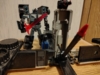 RID Scourge in robot mode, wielding his sword and standing behind his trailer's battle station mode. Much of the battle station is out of frame but a large missile in the center is prominent.